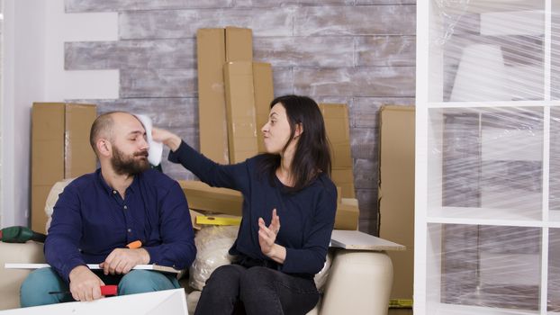 Girlfriend hitting boyfriend with instructions while assembling furniture in their new apartment.