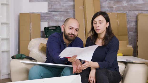 Angry girlfriend hitting boyfriend with furniture instructions. Couple assembling furniture in new apartment.