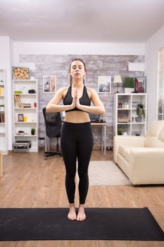 Beautiful young woman practicing yoga for her wellbeing in living room.