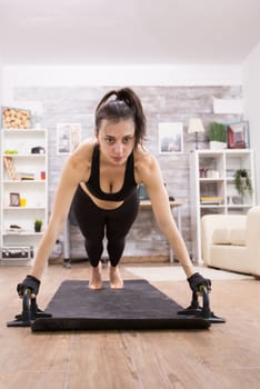 Attractive young woman doing push ups with support in living room.
