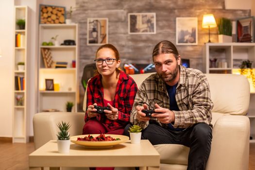 Gamers couple playing video games on the TV with wireless controllers in hands.