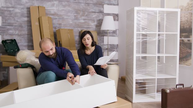 Couple smiling while assembling a shelf as a team and reading instructions.