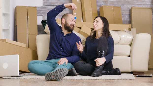 Beautiful young couple sitting on the floor of their new apartment. Boyfriend giving keys to her girlfriend. Cardboard boxes.