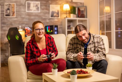 Gamers couple playing video games on the TV with wireless controllers in hands.