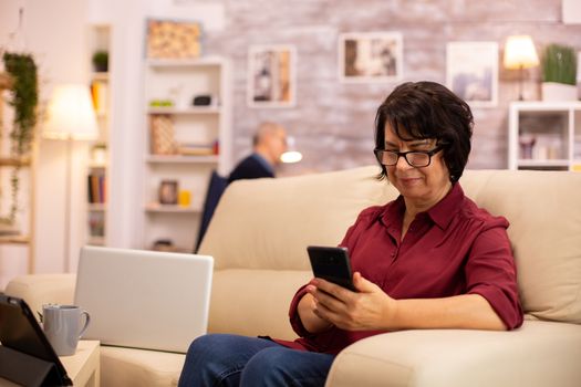 Elderly lady using modern technology in her house. She has a modern smartphone in her hands