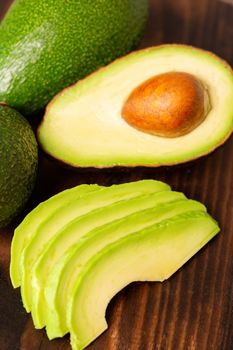 Avocado slices next to cutted one on a wooden board.