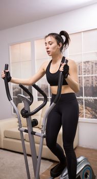 Caucasian young woman doing a strong workout on ellipsoid at home.