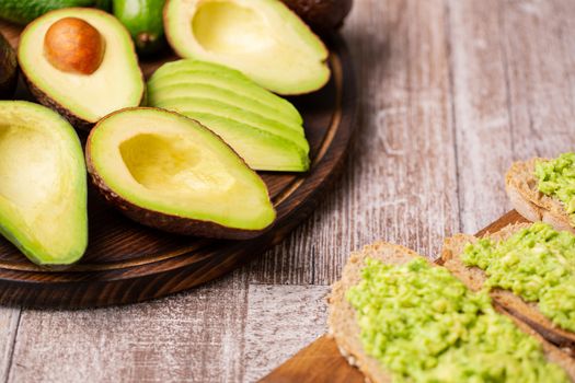 Avocado sandwiches next to cutted ones on wooden board.