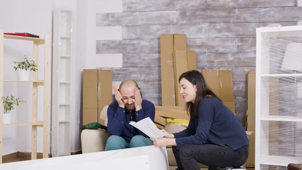 Young couple laughing while assembling furniture in their apartment. Girl reading instructions.