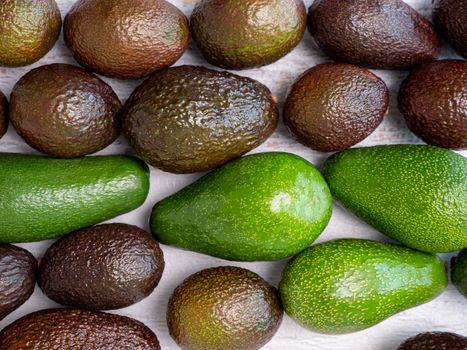 Mix of ripped and green avocados on white wooden board.