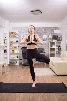 Beautiful young woman with eyes closed practicing tree yoga pose standing in one leg.