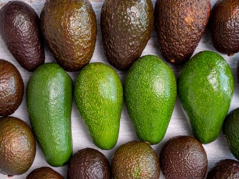 Mix of ripped and green avocados on white wooden board.