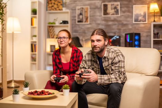 Gamers couple playing video games on the TV with wireless controllers in hands.