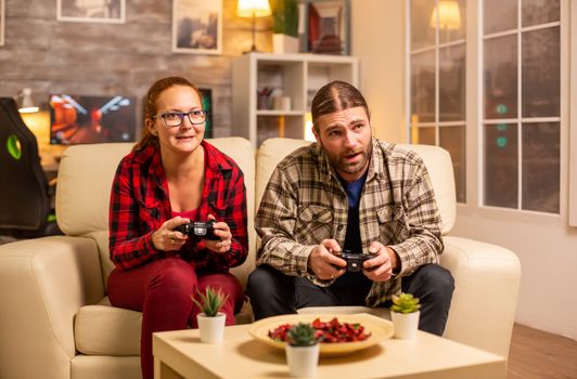 Gamers couple playing video games on the TV with wireless controllers in hands.