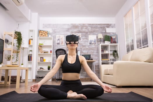 Caucasian young woman doing yoga in living room and wearing virtual reality goggles.