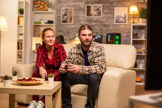 Gamers couple playing video games on the TV with wireless controllers in hands.