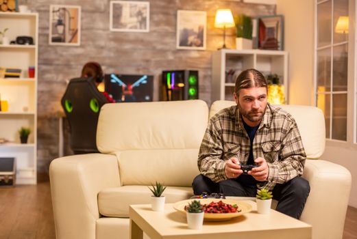 Male gamer playing video games on a console in the living room while sitting on the sofa