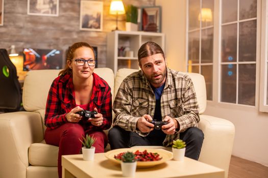 Gamers couple playing video games on the TV with wireless controllers in hands.