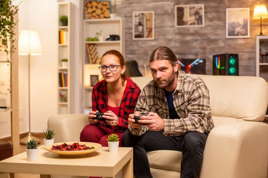 Gamers couple playing video games on the TV with wireless controllers in hands.