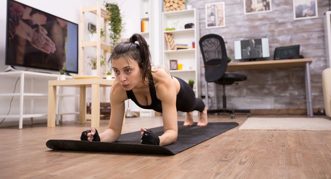 Caucasian beautiful woman doing plank training at home wearing black sportswear.