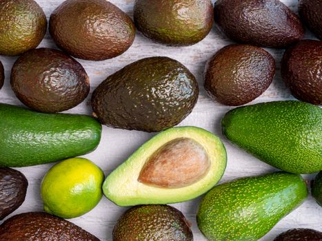 Mix of ripped and green avocados on white wooden board.