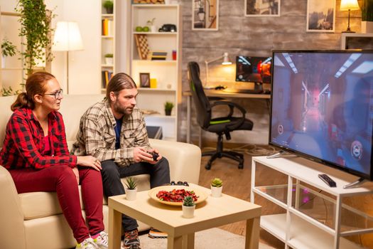 Couple playing video games on big screen TV in the living room late at night.