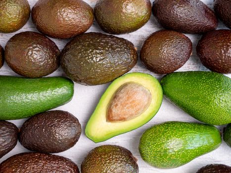 Mix of ripped and green avocados on white wooden board.