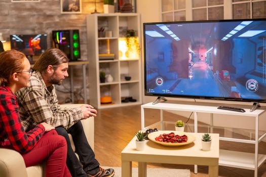 Couple playing video games on big screen TV in the living room late at night.