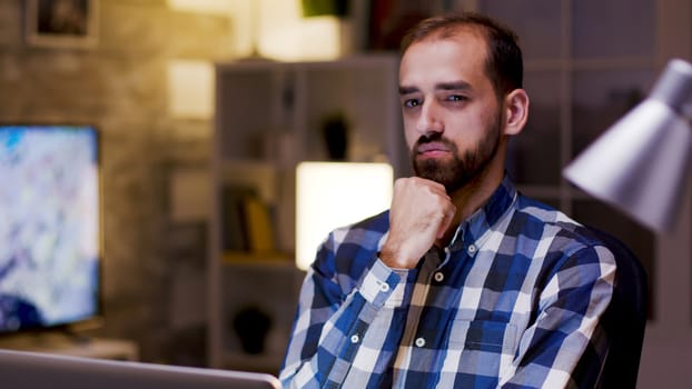 Caucasian entrepreneur thinking while working on his laptop during night hours in his home office.