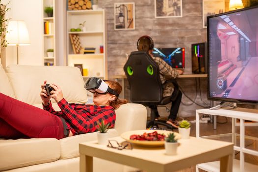 Woman lying on the sofa late at night in living room playing video games using a virtual reality headset