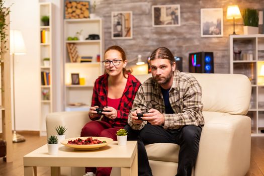 Gamers couple playing video games on the TV with wireless controllers in hands.