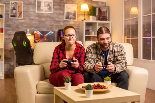 Gamers couple playing video games on the TV with wireless controllers in hands.