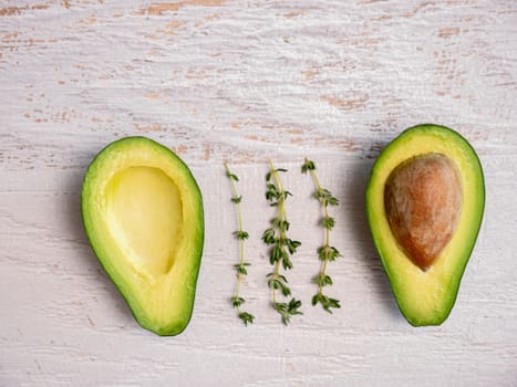 Avocado cut in half on white wooden board.