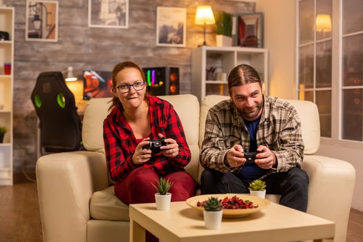 Gamers couple playing video games on the TV with wireless controllers in hands.