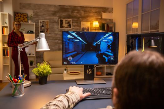 Back view of professional video gamer playing on powerful PC late at night in the living room.