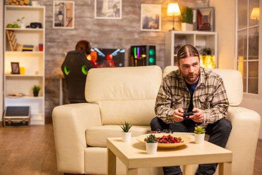 Male gamer playing video games on a console in the living room while sitting on the sofa