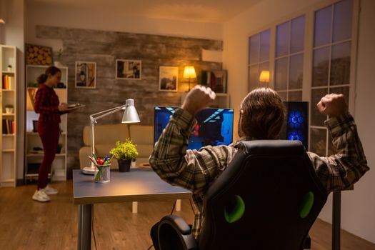 Back view of professional video gamer playing on powerful PC late at night in the living room.