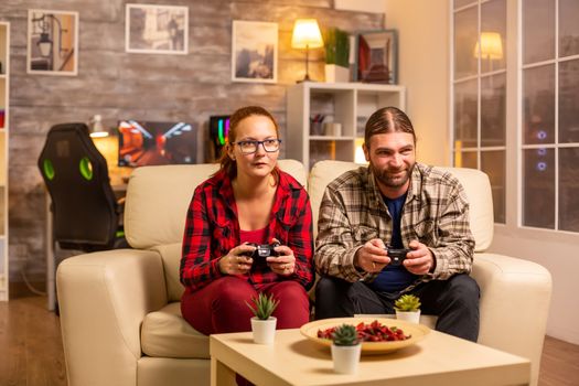 Gamers couple playing video games on the TV with wireless controllers in hands.
