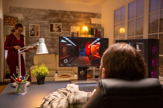 Back view of professional video gamer playing on powerful PC late at night in the living room.