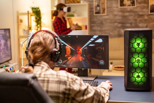 Back view of professional video gamer playing on powerful PC late at night in the living room.