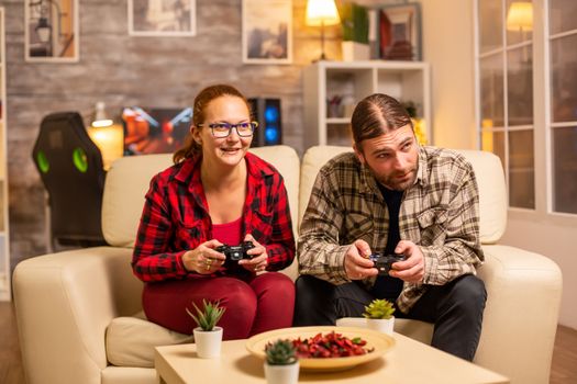 Gamers couple playing video games on the TV with wireless controllers in hands.