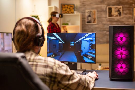 Back view of professional video gamer playing on powerful PC late at night in the living room.