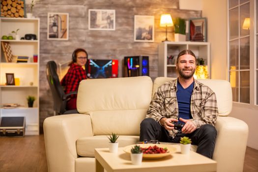 Male gamer playing video games on a console in the living room while sitting on the sofa