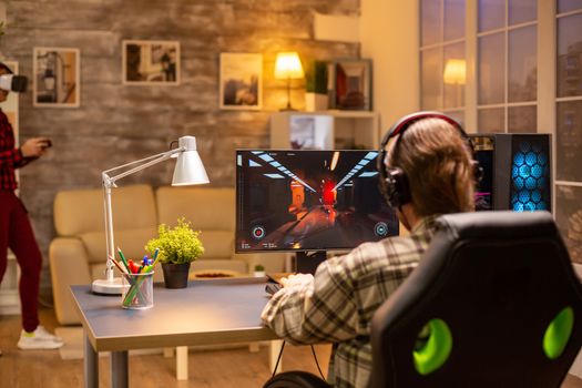 Back view of professional video gamer playing on powerful PC late at night in the living room.