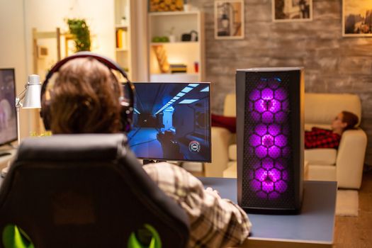 Back view of gamer male playing a shooter on his powerful PC computer late at night in the living room.