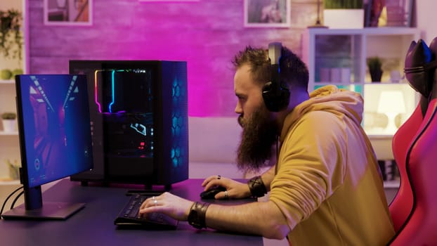Professional game player wearing headphones in a room with colorful neons while playing online video games.