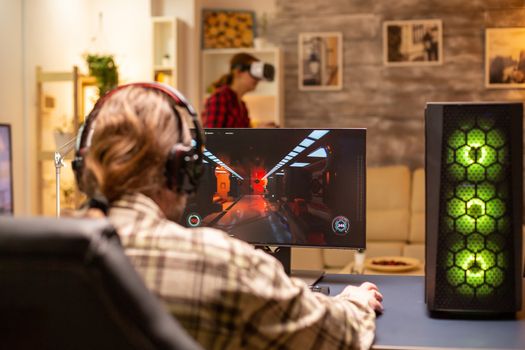 Back view of professional video gamer playing on powerful PC late at night in the living room.