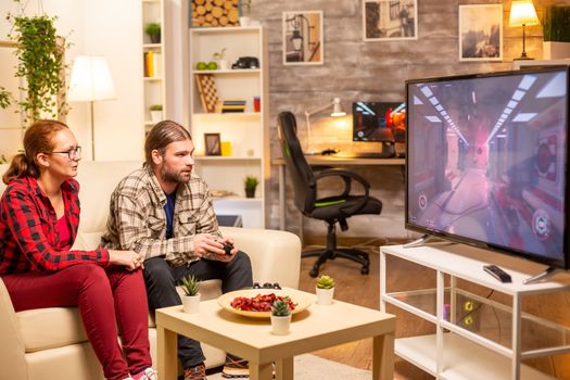 Couple playing video games on big screen TV in the living room late at night.