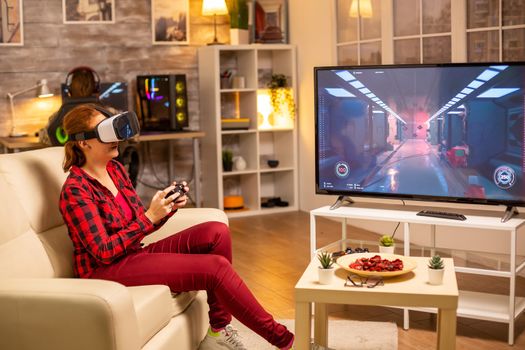 Woman gamer playing video games using a VR headset late at night in the living room