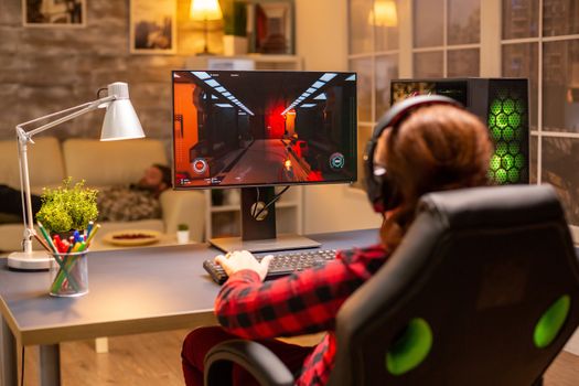 Back view of female gamer playing on powerful computer PC late at night in the living room.